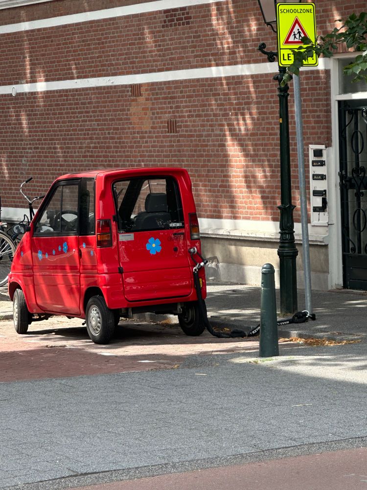 Tiny red car chained to a road sign. 