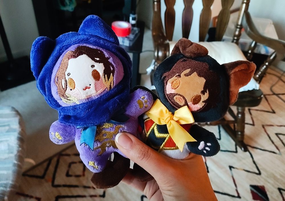 Photo of season 2 ravine Jayce and commune Viktor plushies, called "goodnight babies", by NobleDemons. They have little pet ears and paws. They are about 4 inches tall. I'm holding them in one hand