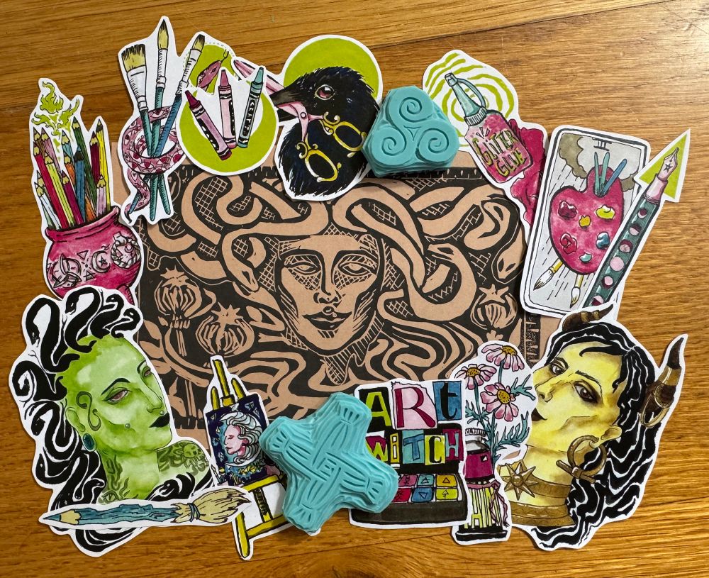 A very cool Medusa Lino print in black ink on Kraft paper. It is framed by two hand carved stamps (one triple spiral, and one St Brigid’s cross), and array of colourful stickers in La Green Witch’s signature bold, playful, and witchy style.