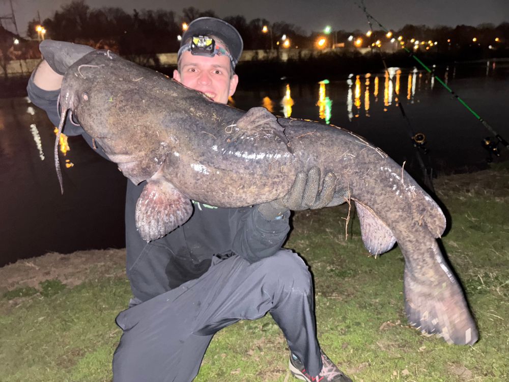 I am kneeling down and holding out the large flathead catfish 