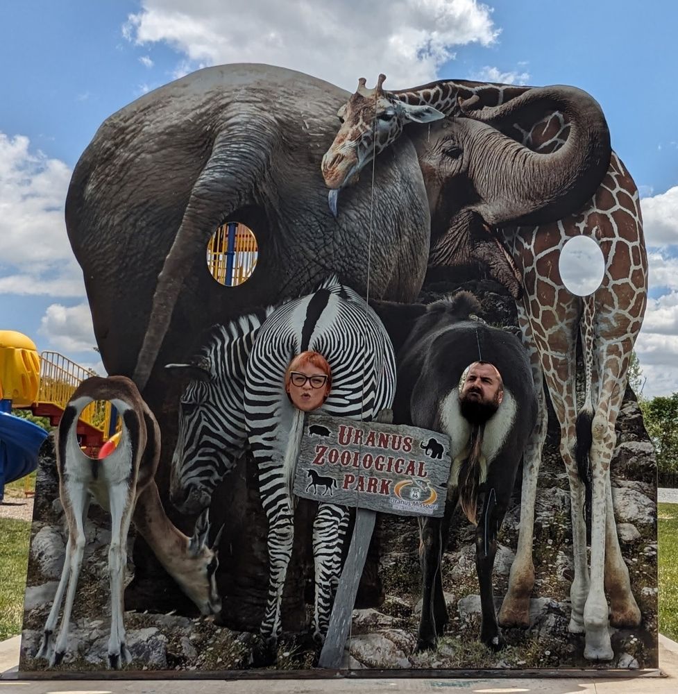 A photo of benchly and his wife poking their faces through a wooden cutout that depicts a bunch of animal rumps. The holes where your head comes through is very conveniently located at the butthole, because sometimes things just work out that way.