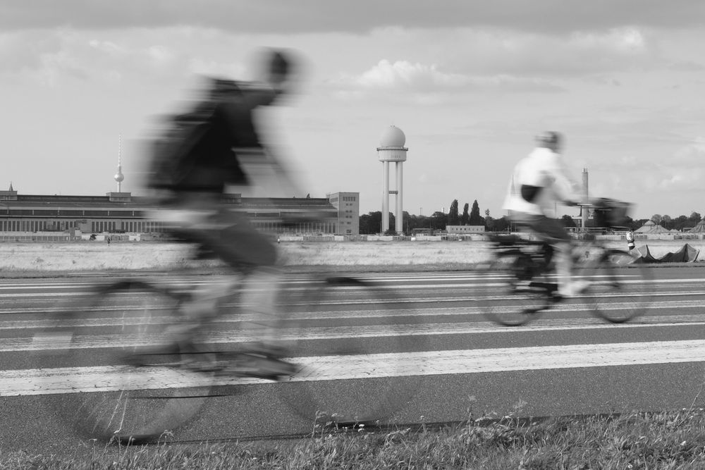 Two cyclists in front of the airport tower of Tempelhofer Feld. 