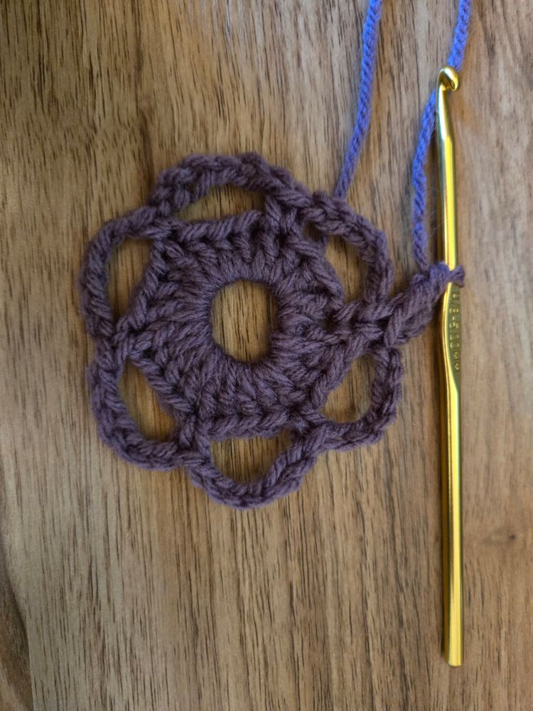 Crochet practice in a purple lace round with a gold crochet hook.