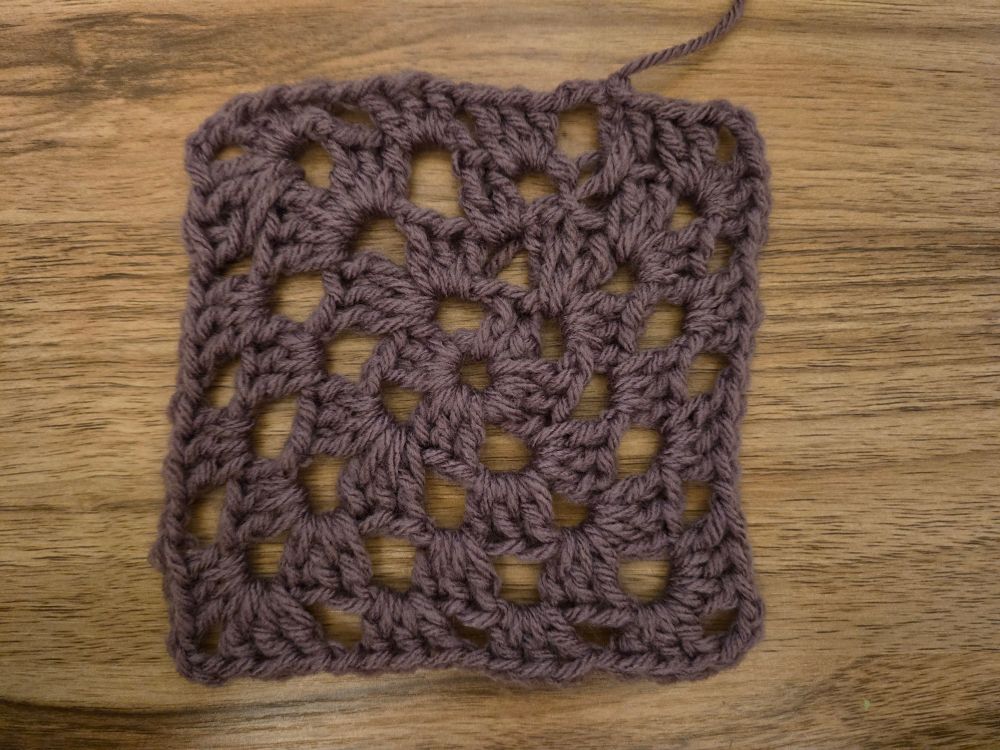 Purple yarn crocheted granny square on a desk.