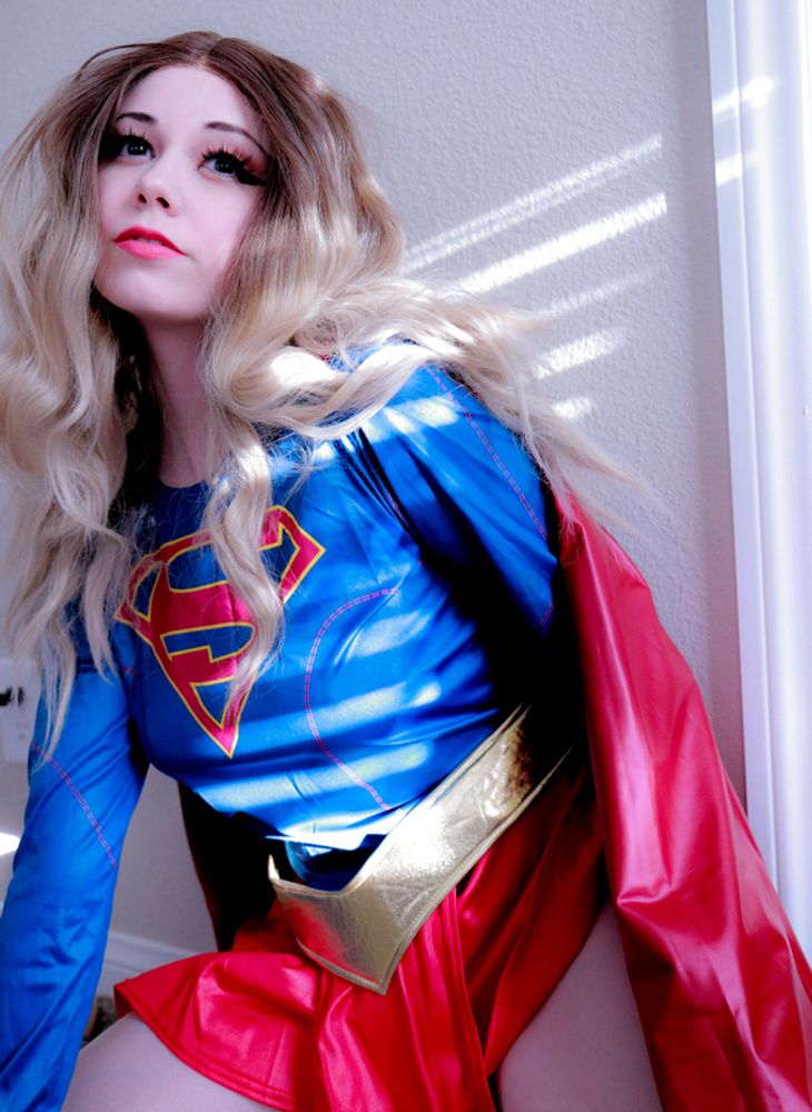 Runesy wearing a supergirl cosplay with long brown hair, and rays of sunlight glowing on her. 
