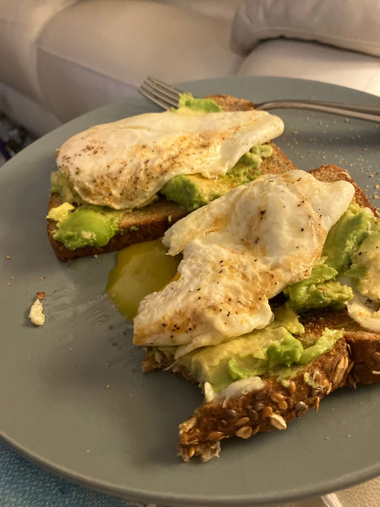 Two slices whole grain bread with avocado and jammy eggs on top. 