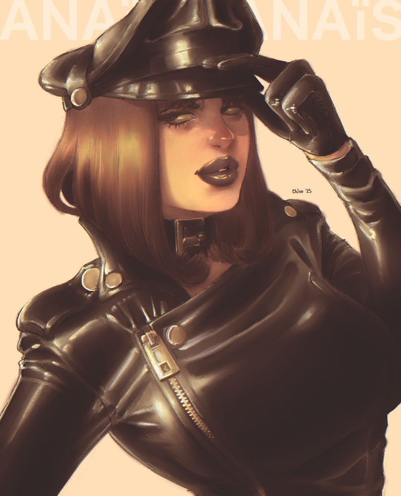 Anaïs with her signature brown bob wearing a tight black leather jacket, black leather gloves, black leather Muir cap, and collar, left hand up to the brim of her cap.