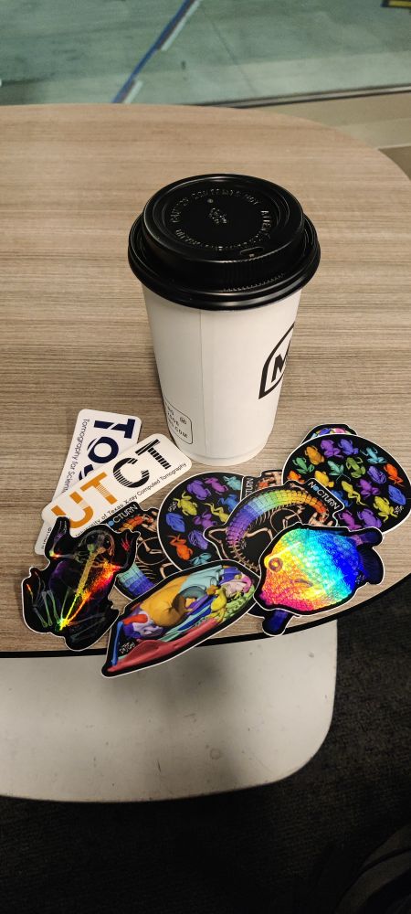 A coffee cup sitting on a table at an airport. Next to the coffee cup lies a pile of colorful stickers showcasing 3D renderings of CT scans