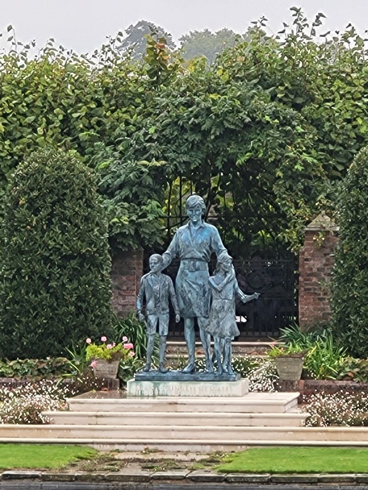 A statue of Diana Princess of Wales with 3 children stand in the sunken garden of Kensington Palace