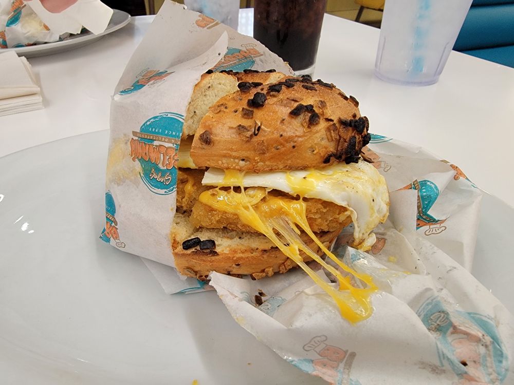 An onion bagel sandwich filled with a fried egg, melting cheddar cheese, and a hashbrown patty. 