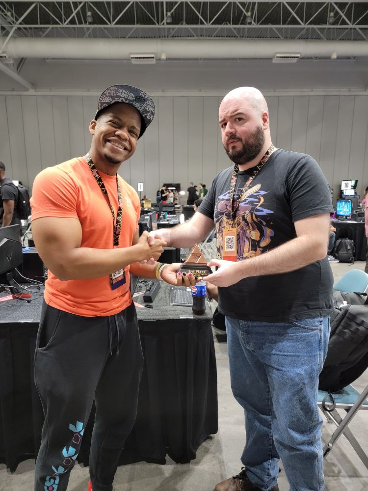 Ryyudo proudly smiling and handing the Triforce trophy over to Cocojam, looking concerned and confused as they engage in a handshake with the other hand. 