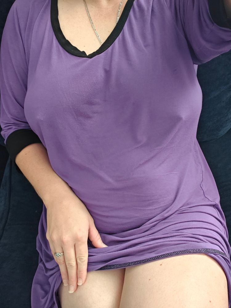 A body shot of myself sitting on my couch wearing a purple night dress with black trim. My hand is resting on my leg with my dress pulled up