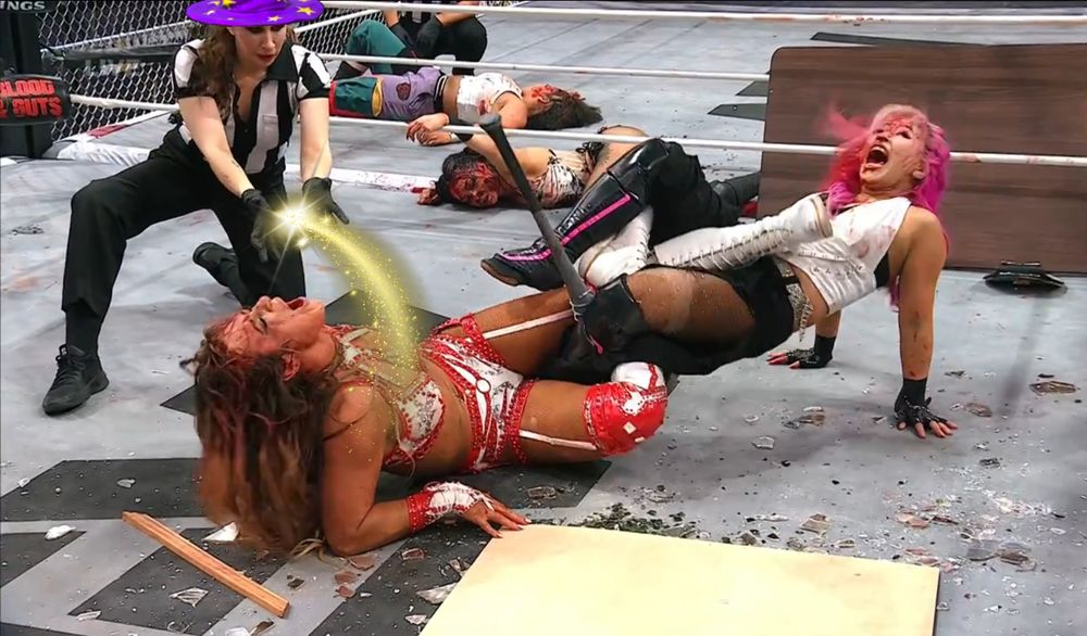 AEW referee Aubrey Edwards wearing a wizard hat with golden magic emitting from her hands onto Megan Bayne, who is down on the mat in a figure four with a barb wire baseball bat intertwined in her legs.