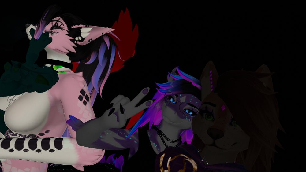 Three brightly colored anthropomorphic VRChat avatars pose together in the dark, one making a peace sign, with neon-accented fur and hair illuminated against a black background.