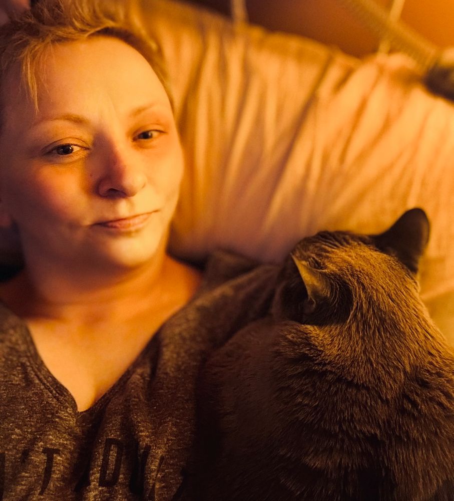 selfie of me lying in bed with my chonky blue point Siamese kitty Sven draped over my left shoulder, dead asleep 