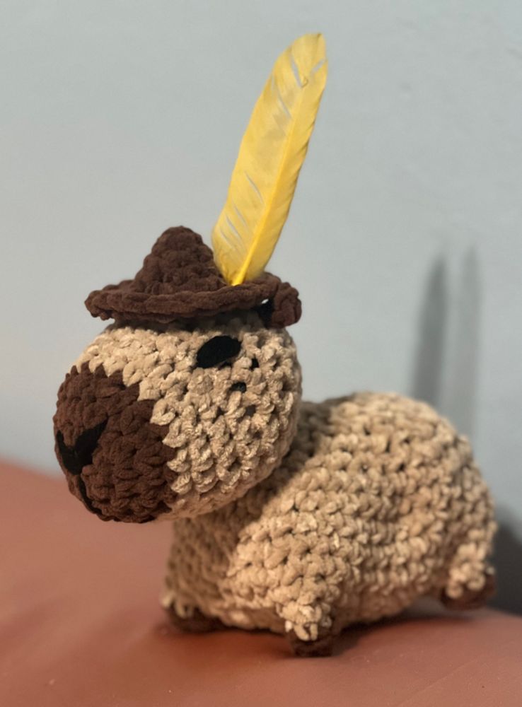 Crocheted capybara with brown hat and yellow feather