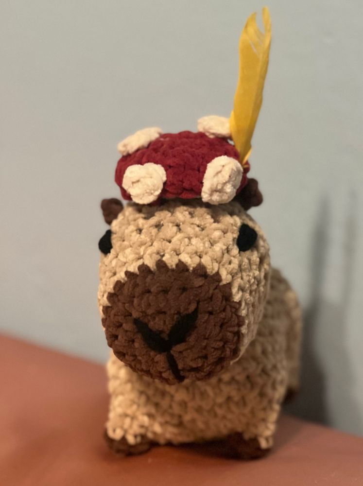 Crocheted capybara with mushroom hat and yellow feather