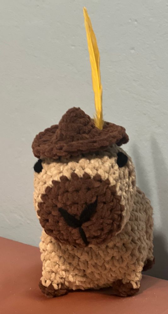 Crocheted capybara with brown hat and yellow feather 