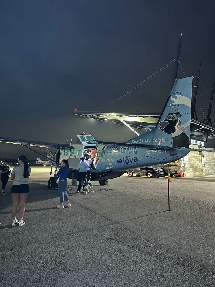 The plane in full view as it’s being loaded! On the side of it, there’s text that reads “Dog Is My CoPilot” with an illustration of a dog with their face in the wind on the plane’s tail.