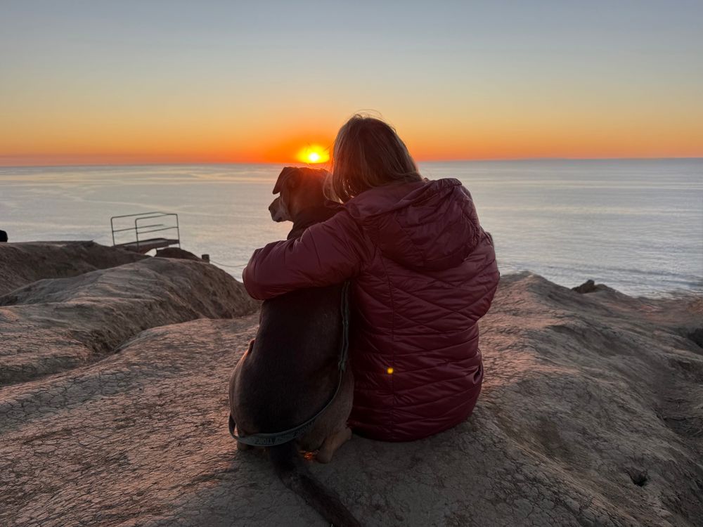 Rachel admires a sunset at the beach with Hugs by her side.