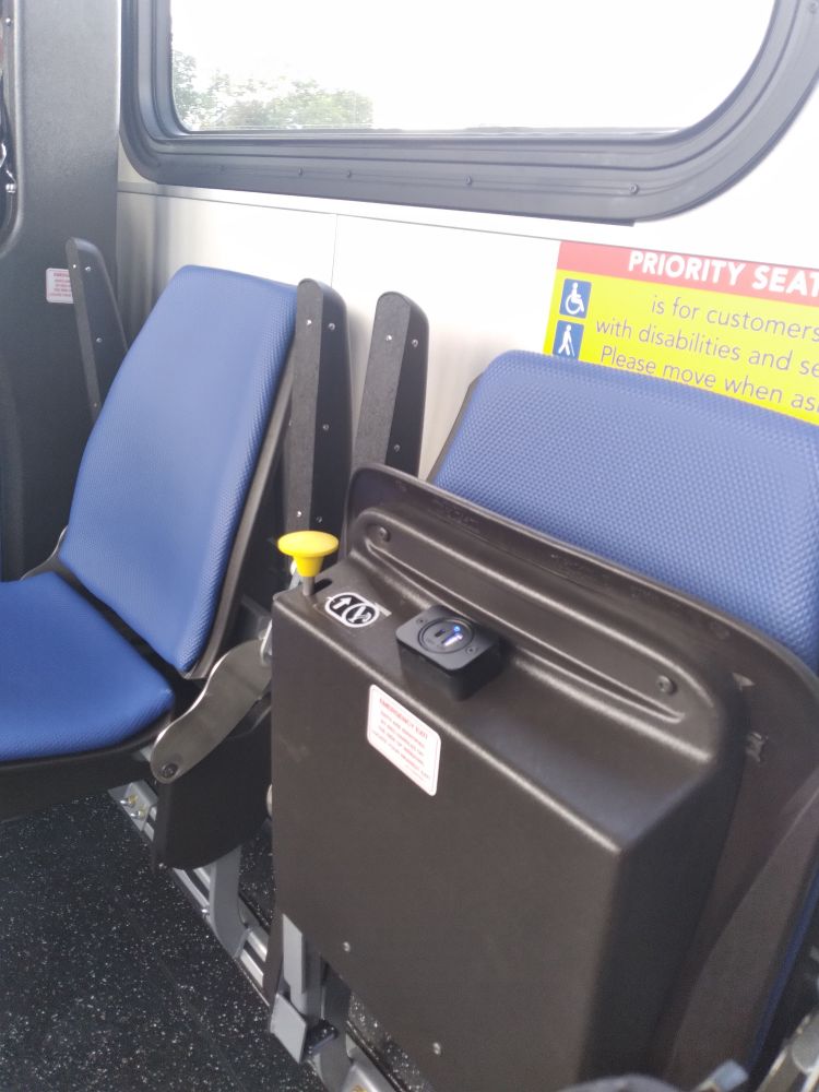 2 textured vinyl blue bus seats. One is flipped up to show the charging port built into the seat.
