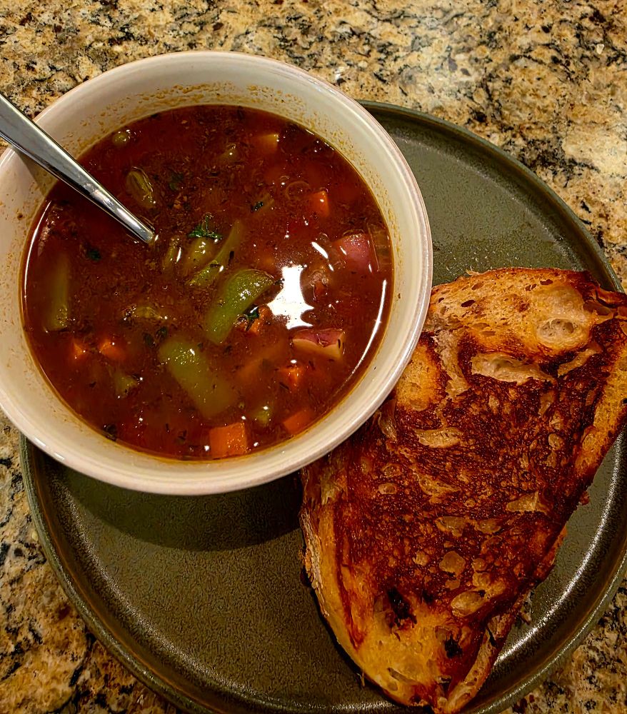 a bowl of beef vegetable soup on a plate with a cheese toastie