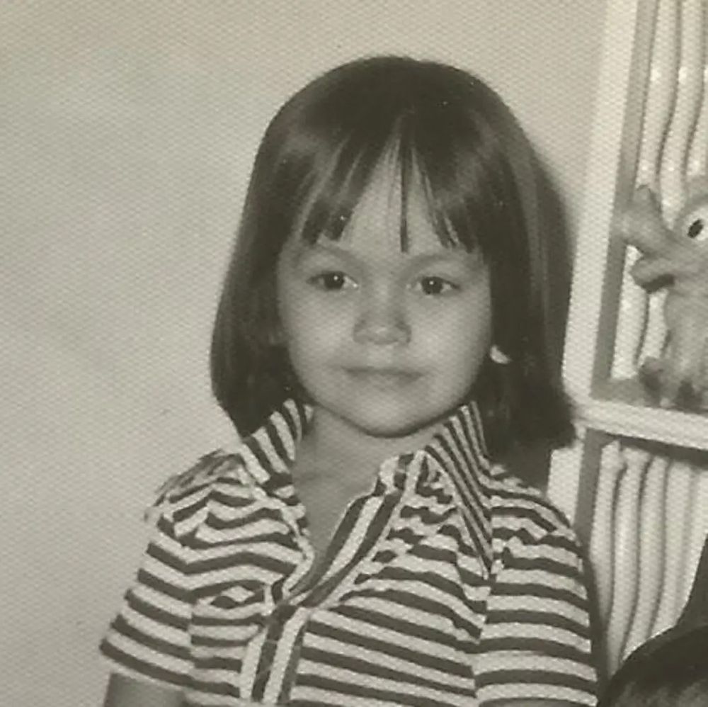 Minha foto criança em preto e branco. Tenho uns 3 anos. Uso cabelos compridos lisos e longos e camisa com gola listrada em preto e branco. 