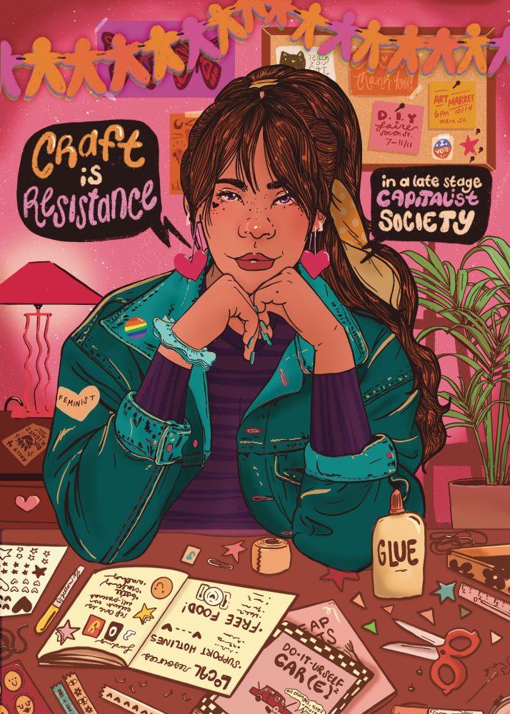 digital illustration of a woman with long brown hair wearing a jean jacket and purple sweater. She’s sitting at a craft table with zine making supplies. Text reads, ‘craft is resistance in a late stage capitalist society.’