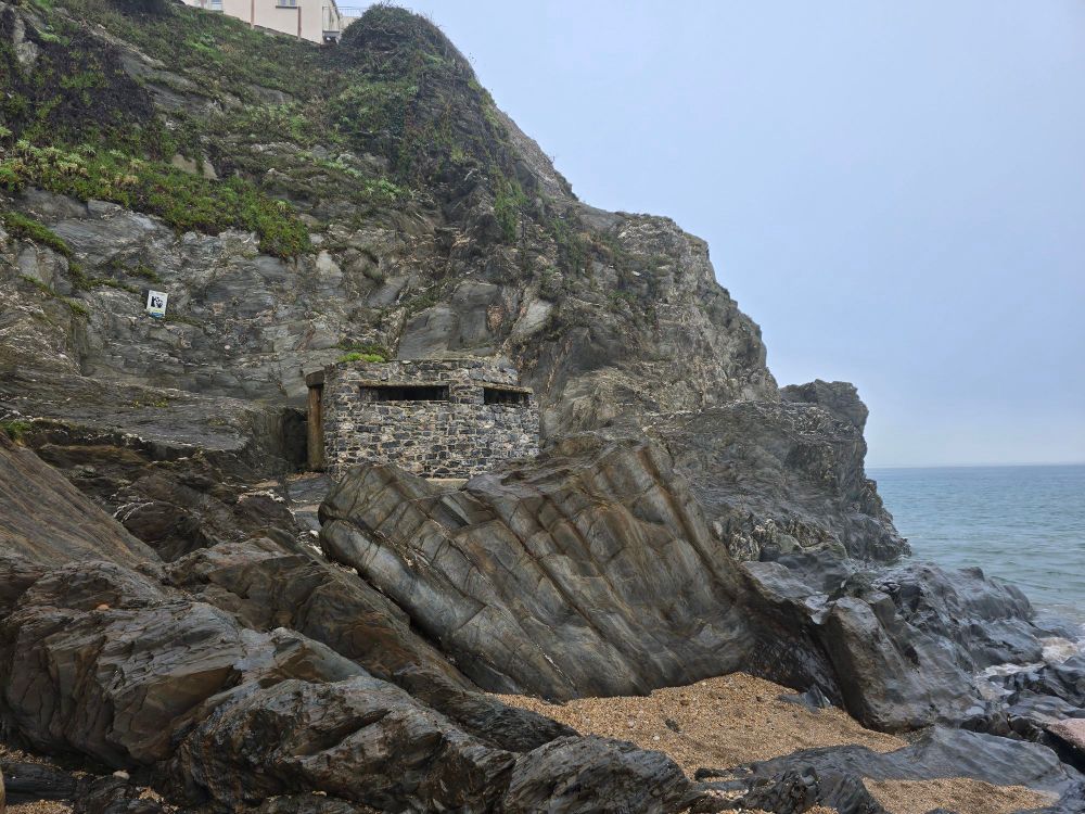 A stone pillbox above a beach in Devon, England, with a cliff behind it
