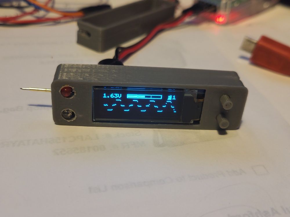 Small grey 3d printed box on white desktop showing 1.6v and a squared off AC waveform. 