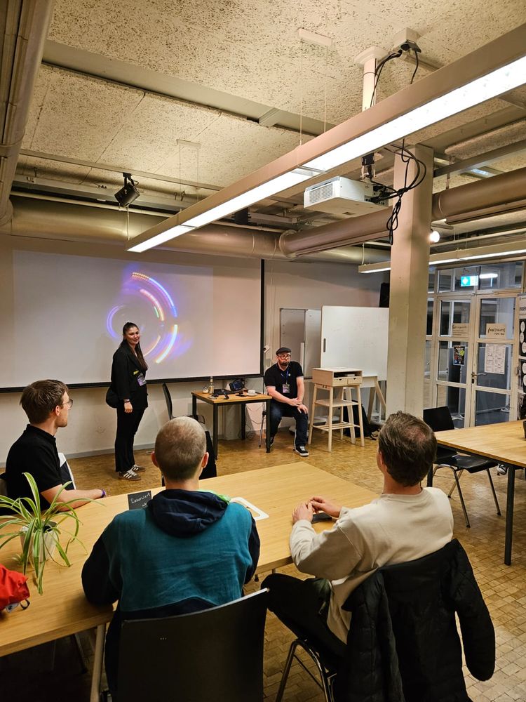 Eine Frau und ein Mann stehen vor einer Leinwand. Davor sitzen Menschen als Publikum.