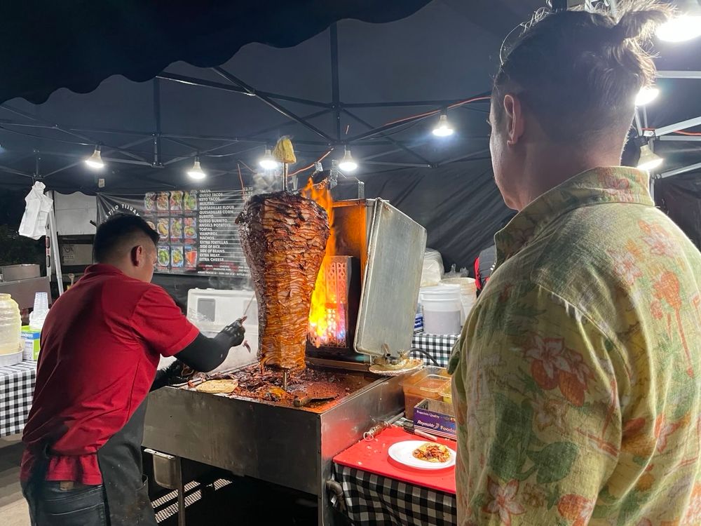 Cook slicing layered meat from a vertical spit in an outdoor kitchen at night.