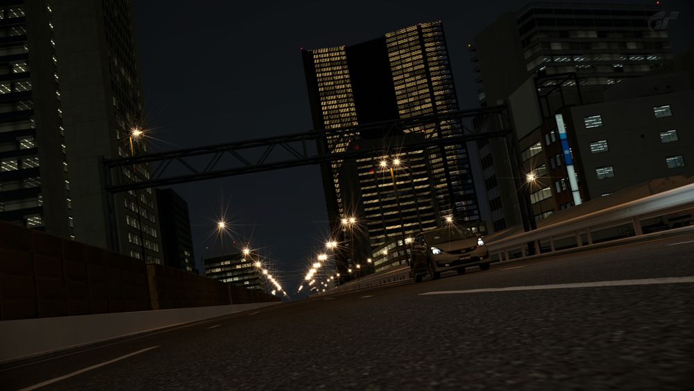 Gran Turismo 6, for the PlayStation 3 (PS3). Special Stage Route 5. A Honda Fit drives on city streets at night. Skyscrapers nearby are lit inside.