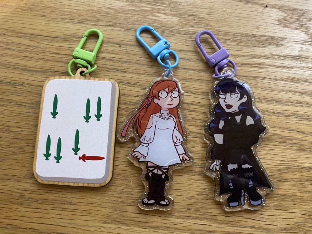 A 7 of Bamboo alongside Ryne and Gaia acrylic charms on a desk.