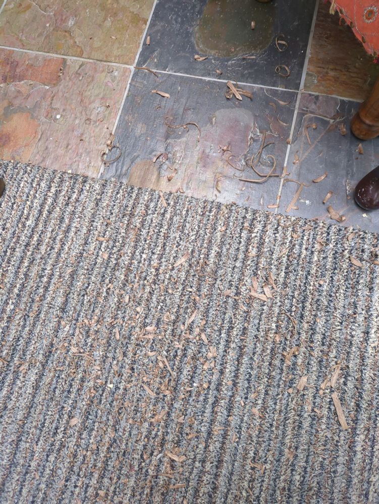 A photo of wood shavings on a rug and on a slate tiled floor