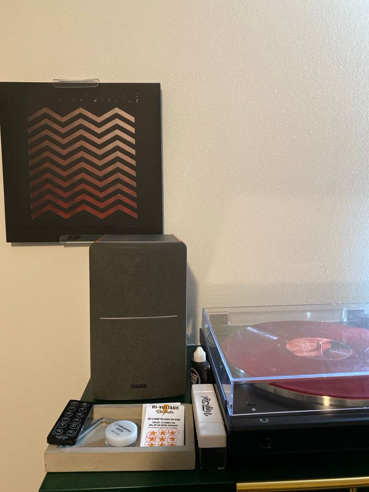 Record player on a shelf with the record “Fire Walk With Me” by Angelo Badalamenti on a white wall