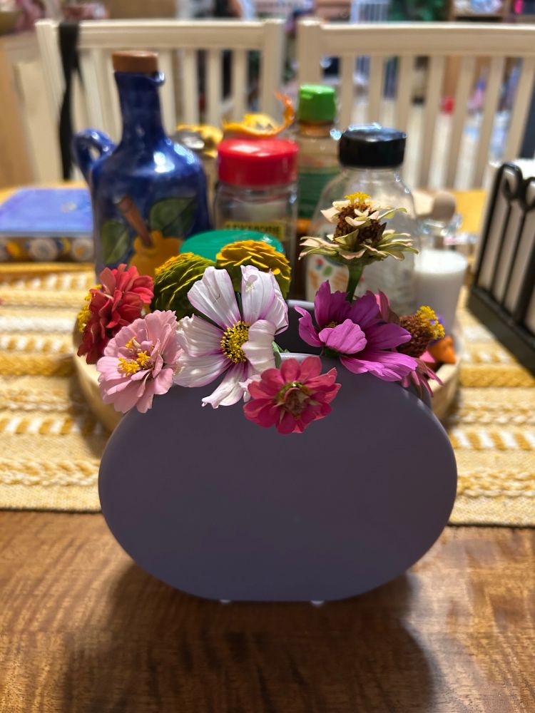 A front facing view of a purple vase full of orange and pink zinnias, and pink cosmos.