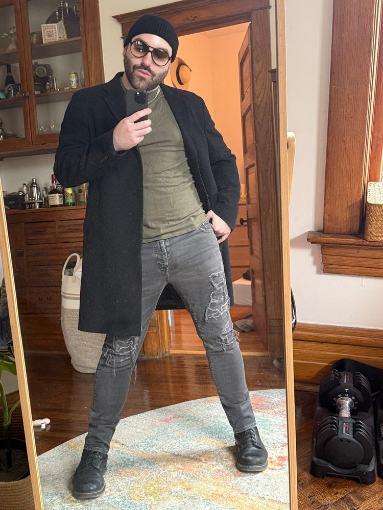 Mirror selfie fit pic. I’m wearing black boots, distressed grey jeans, a black coat and an olive green t-shirt. Also black beanie and a pair of large sunglasses. It was way too cold for this outfit I should have worn a sweater or something but whatever it was cute.