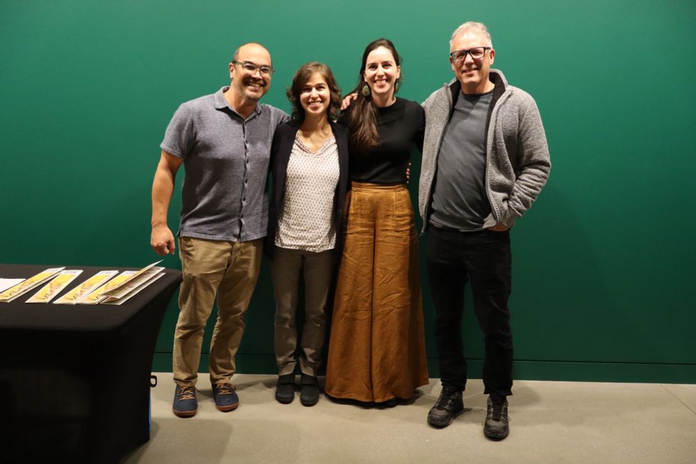 Four people smiling and standing in front of green wall 