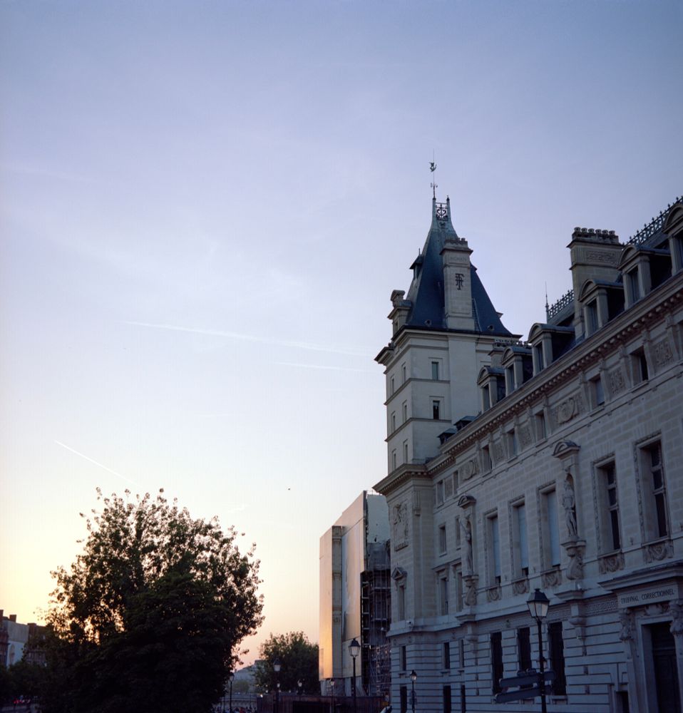 A color photo of the Palais de Justice in Paris at sunset, showing its ornate stone façade and steep tower roof against a pastel sky, with warm light reflecting off nearby scaffolding, taken with a Voigtländer Perkeo II and 80 mm f/3.5 Color-Skopar lens on Kodak Portra 160 film.