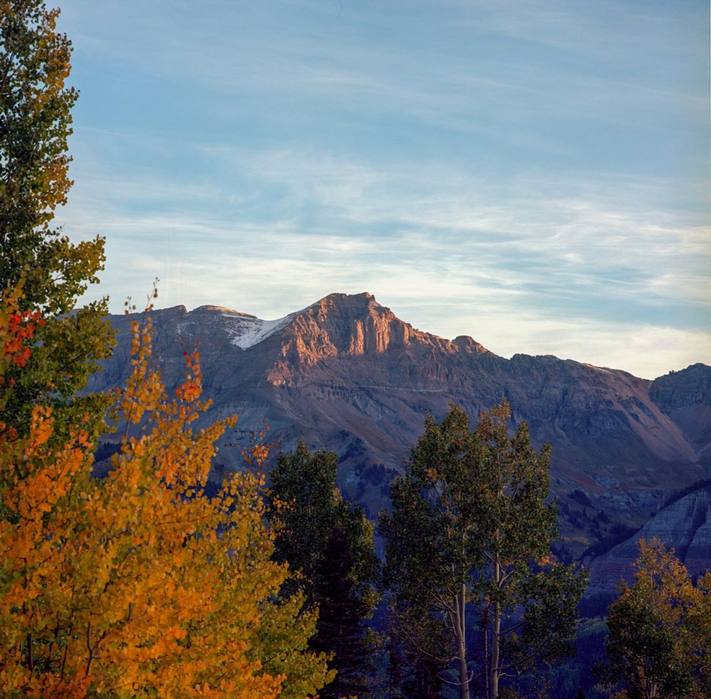 Rugged mountain peak bathed in warm dawn light with autumn-colored aspens in the foreground, photographed with a Mamiya 6 and 50mm lens on Kodak Ektar 100 film.