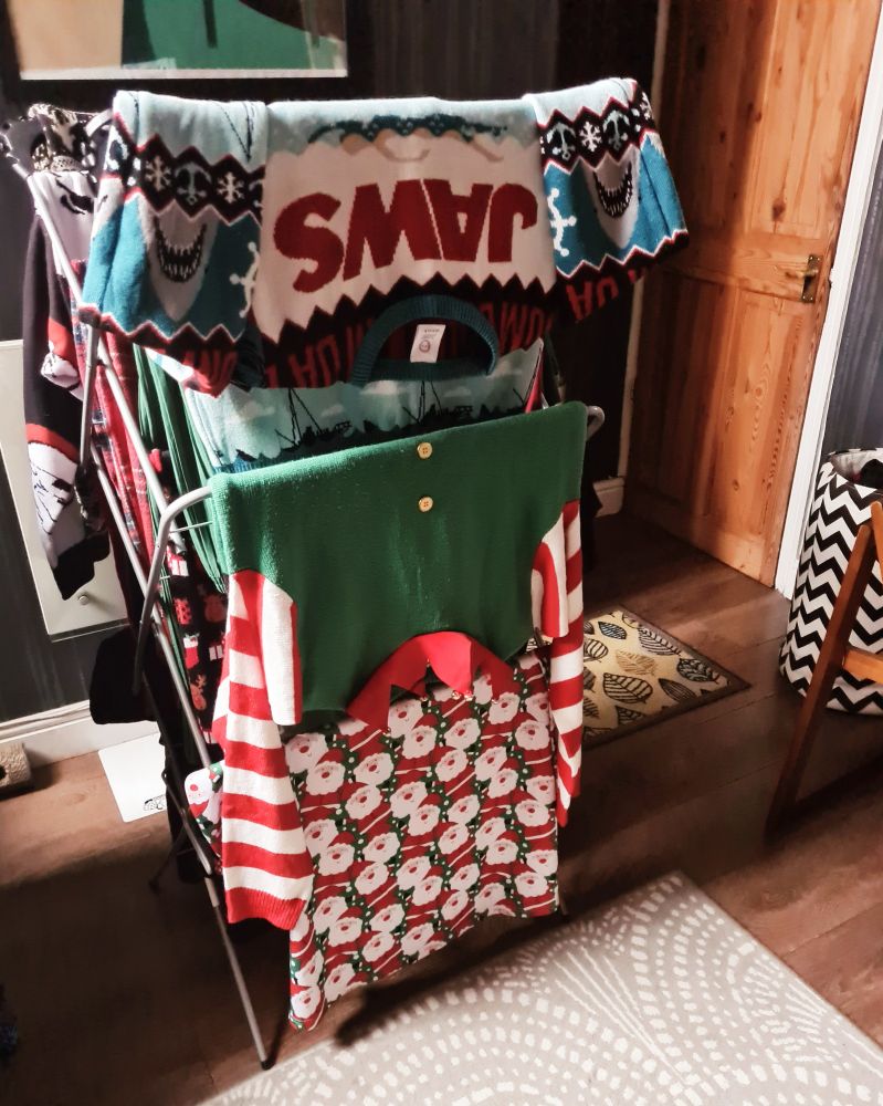 Lots of festive jumpers drying after being washed. A Jaws themed jumper, santa dress and Elf jumper with bells.