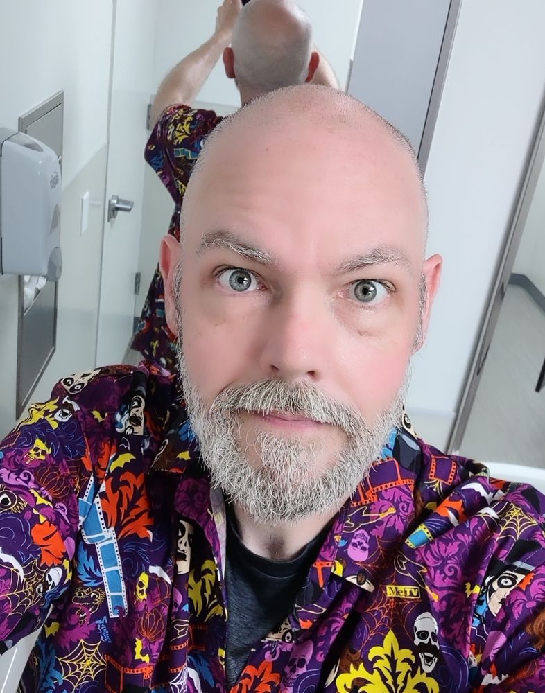 A beautiful, bald, bearded man wearing a sharp, spoopy Svenghoulie shirt