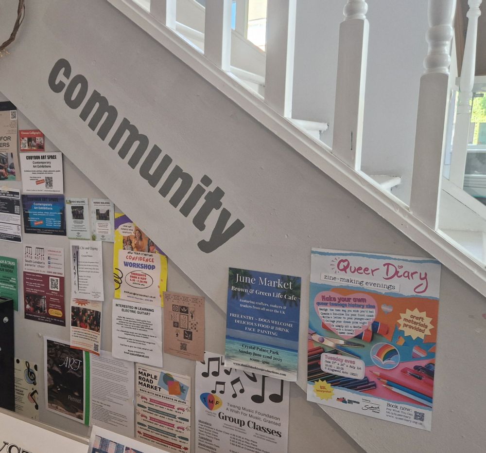A wall full of posters including a queer diary poster alongside local classes, markets, etc, with the word "community" painted above it.