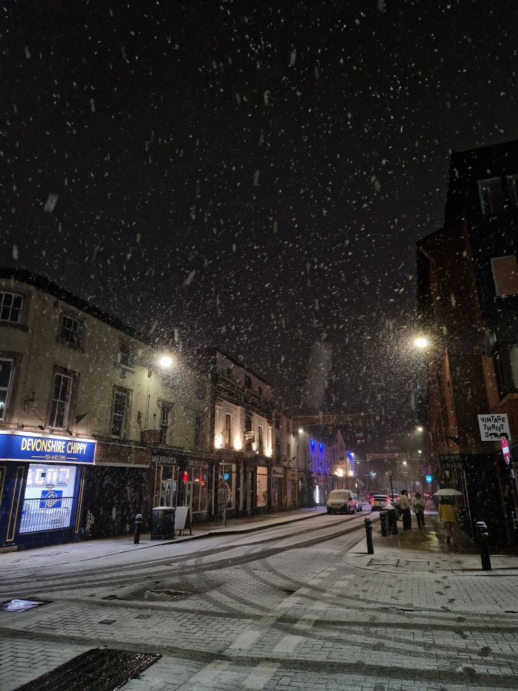 Snow covers a street. Car tracks can be seen in the light coverage.