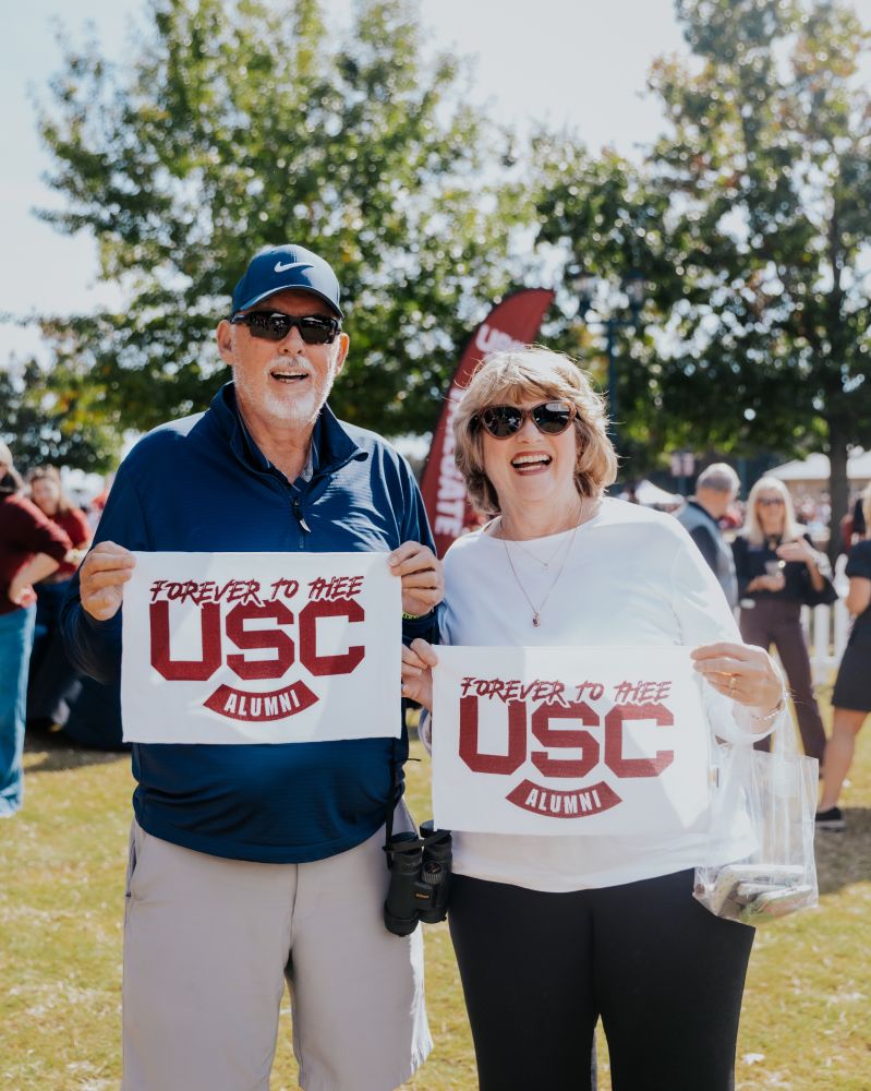 USC Alums pose with rally towels that say "forever to thee, USC alumni"