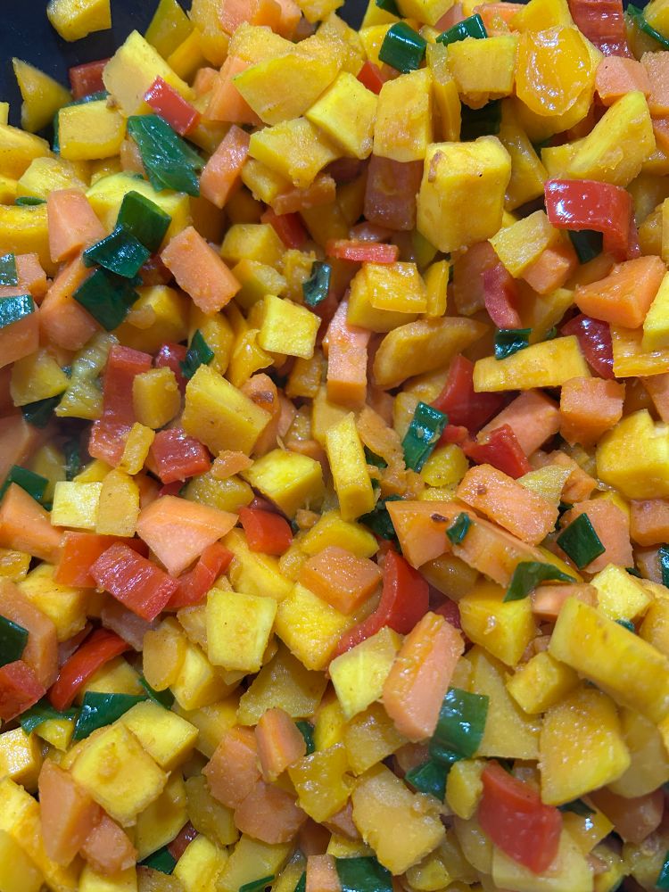 Gerecht in de pan: oranje stukjes pompoen en zoete aardappel, groene bosui en rode en oranje zoete puntpaprika