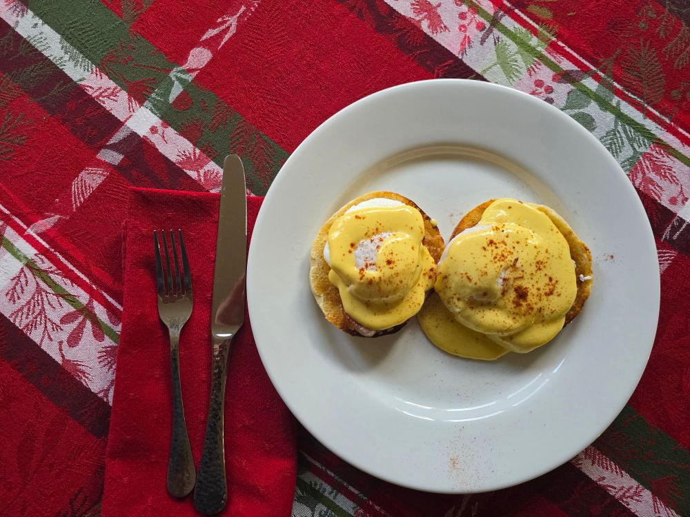 Eggs Benedict on a plate on a table with a holiday tablecloth
