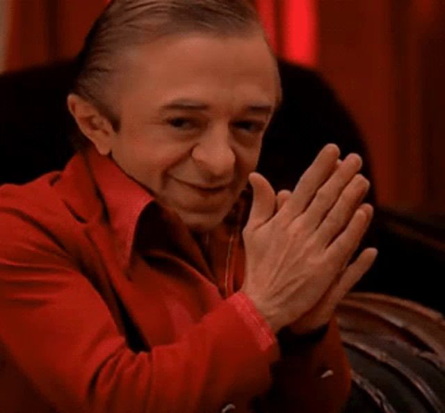 a man in a red suit is clapping his hands while sitting in a chair .