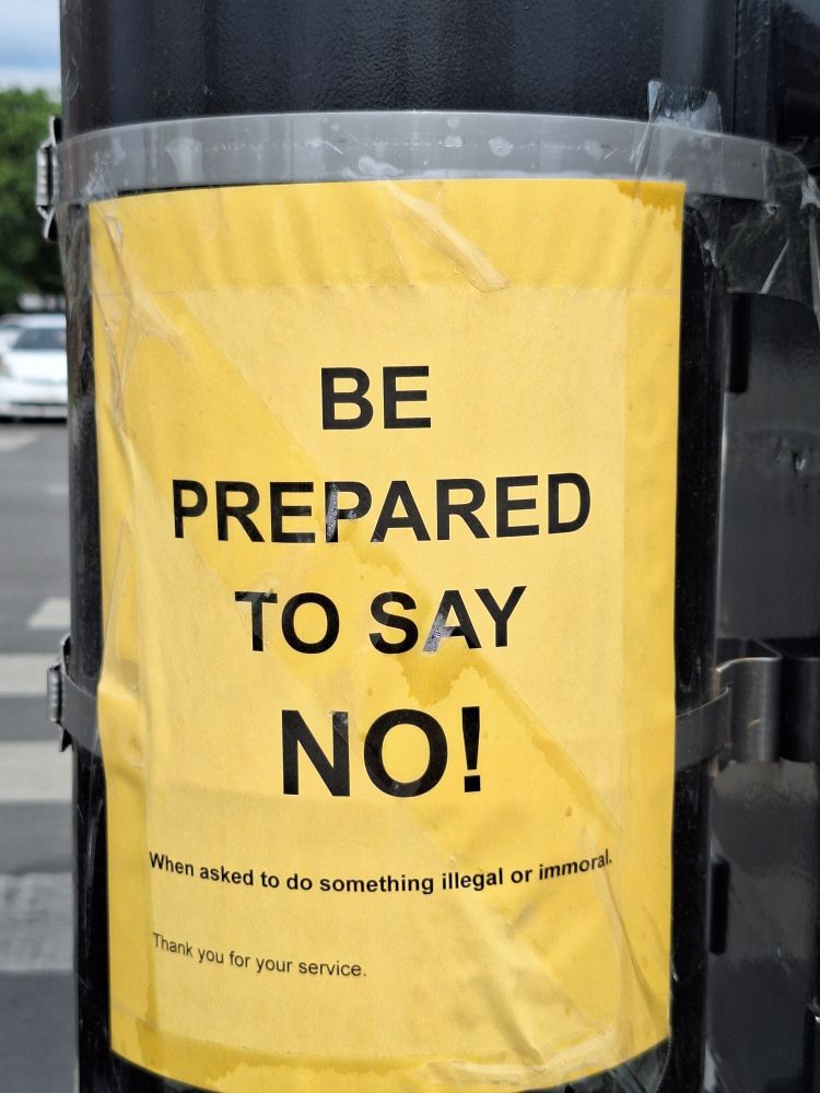 A yellow sign on a traffic pole saying "be prepared to say no! when asked to do something illegal or immoral." 